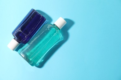 Photo of Bottles of mouthwash on light blue background, top view. Space for text