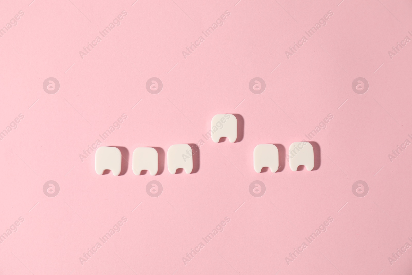 Small teeth figures on pink background, flat lay Photo of Small teeth figures on pink background, flat lay