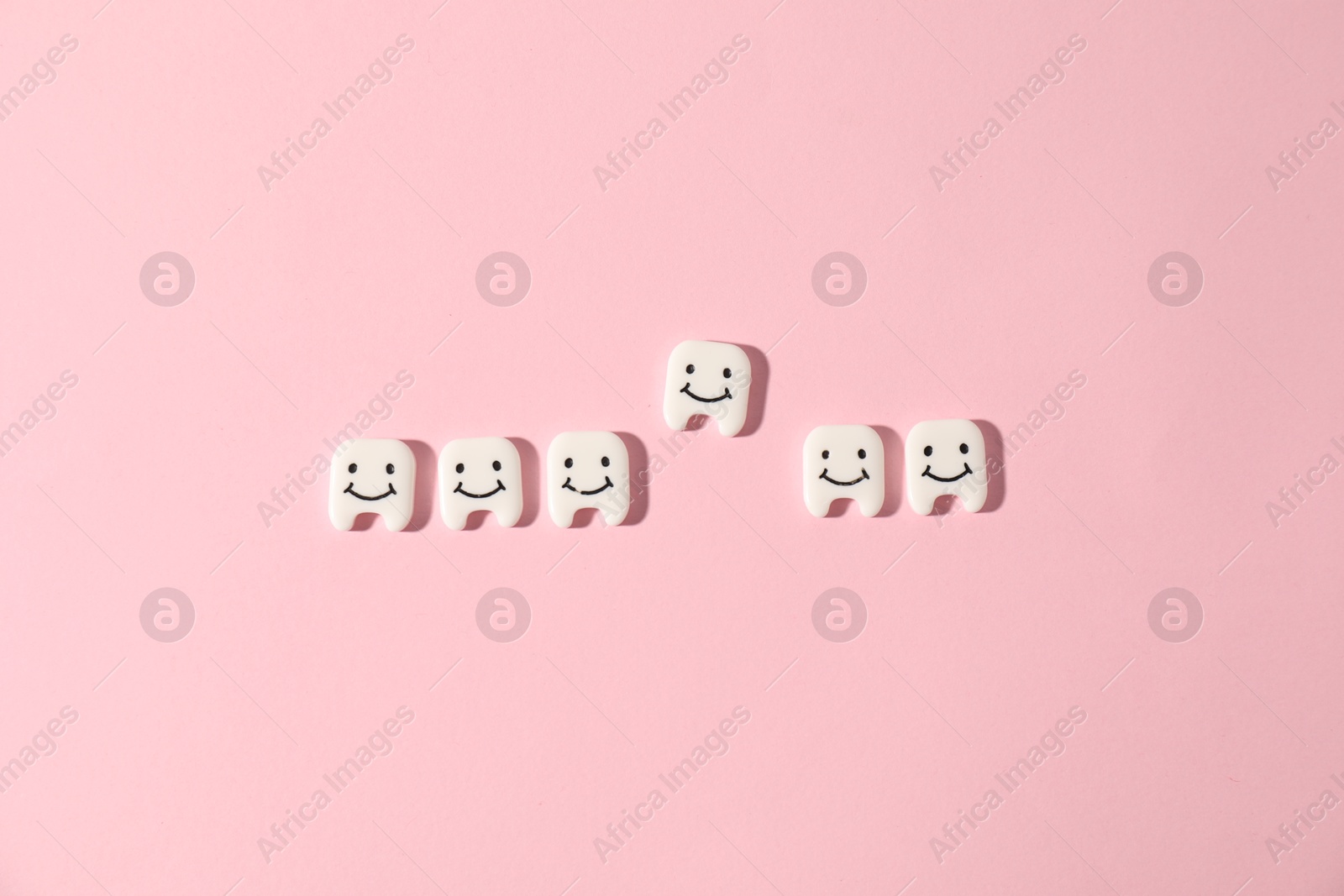Small teeth figures on pink background, flat lay Photo of Small teeth figures on pink background, flat lay