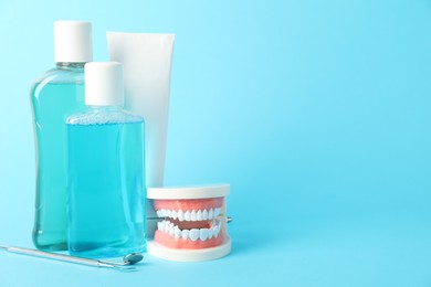 Photo of Different oral care products and dental model on light blue background. Space for text