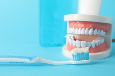 Photo of Dental model, mouthwash and toothbrush with paste on light blue background, closeup
