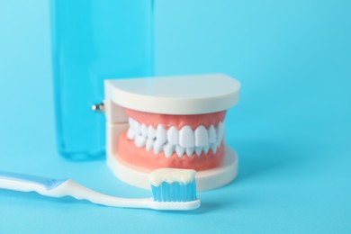 Photo of Dental model, mouthwash and toothbrush with paste on light blue background, closeup