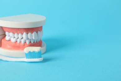 Photo of Dental model and toothbrush with paste on light blue background, closeup. Space for text