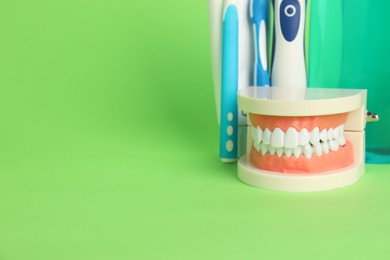 Photo of Different oral care products and dental model on green background, closeup. Space for text