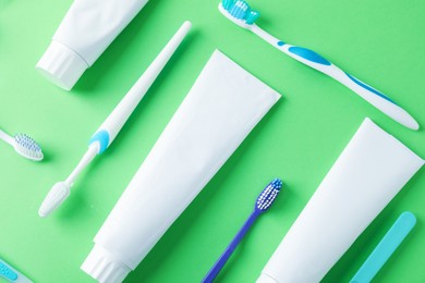 Photo of Toothbrushes and tubes of toothpaste on green background, flat lay
