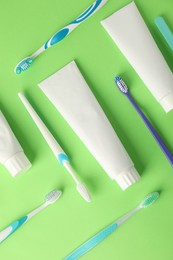 Photo of Toothbrushes and tubes of toothpaste on green background, flat lay
