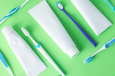 Photo of Toothbrushes and tubes of toothpaste on green background, flat lay
