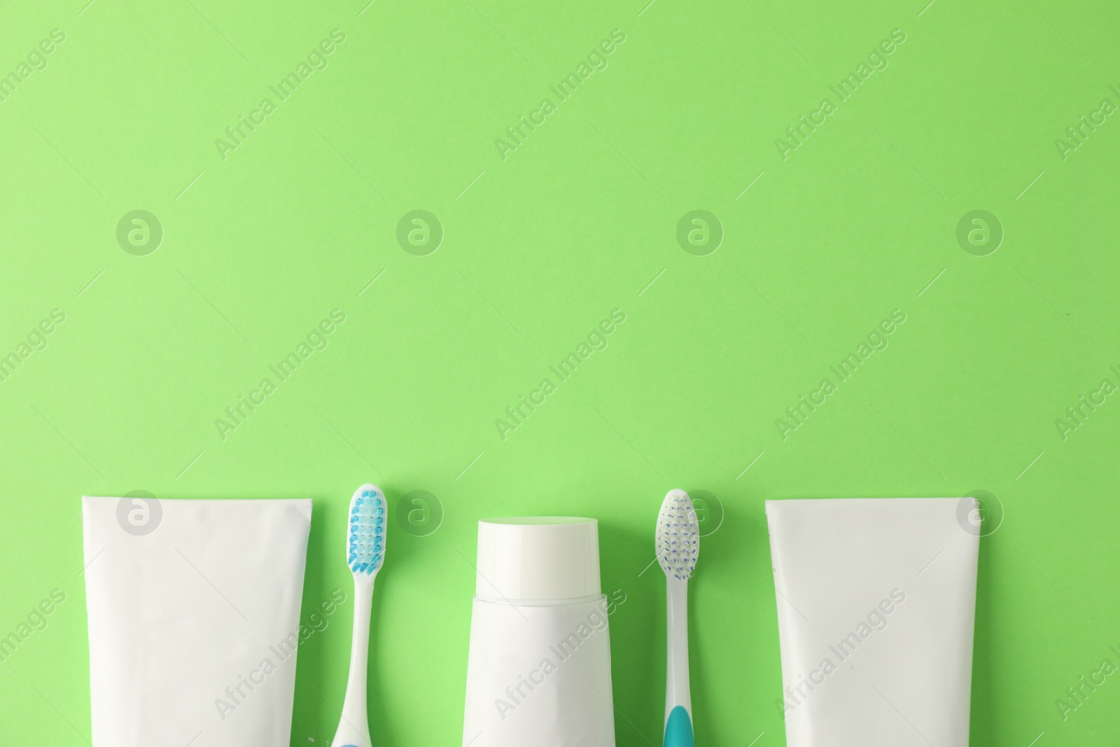 Toothbrushes and tubes of toothpaste on green background, flat lay. Space for text Photo of Toothbrushes and tubes of toothpaste on green background, flat lay. Space for text