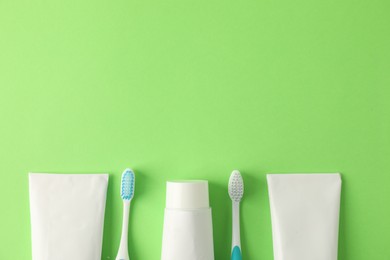 Photo of Toothbrushes and tubes of toothpaste on green background, flat lay. Space for text