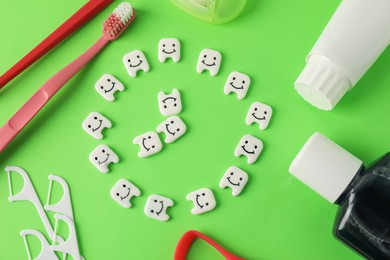 Photo of Different oral care products and teeth figures on green background, flat lay