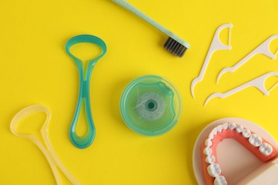 Photo of Different oral care products and dental model on yellow background, flat lay