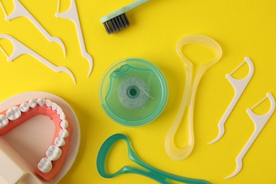 Photo of Different oral care products and dental model on yellow background, flat lay