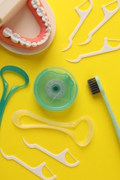 Photo of Different oral care products and dental model on yellow background, flat lay