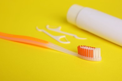 Photo of Toothbrush, toothpaste and floss picks on yellow background, closeup