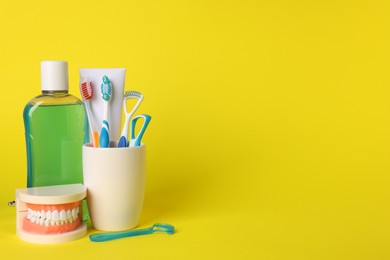 Photo of Different oral care products and dental model on yellow background, space for text
