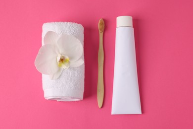 Photo of Toothbrush, toothpaste, towel and orchid flower on pink background, flat lay