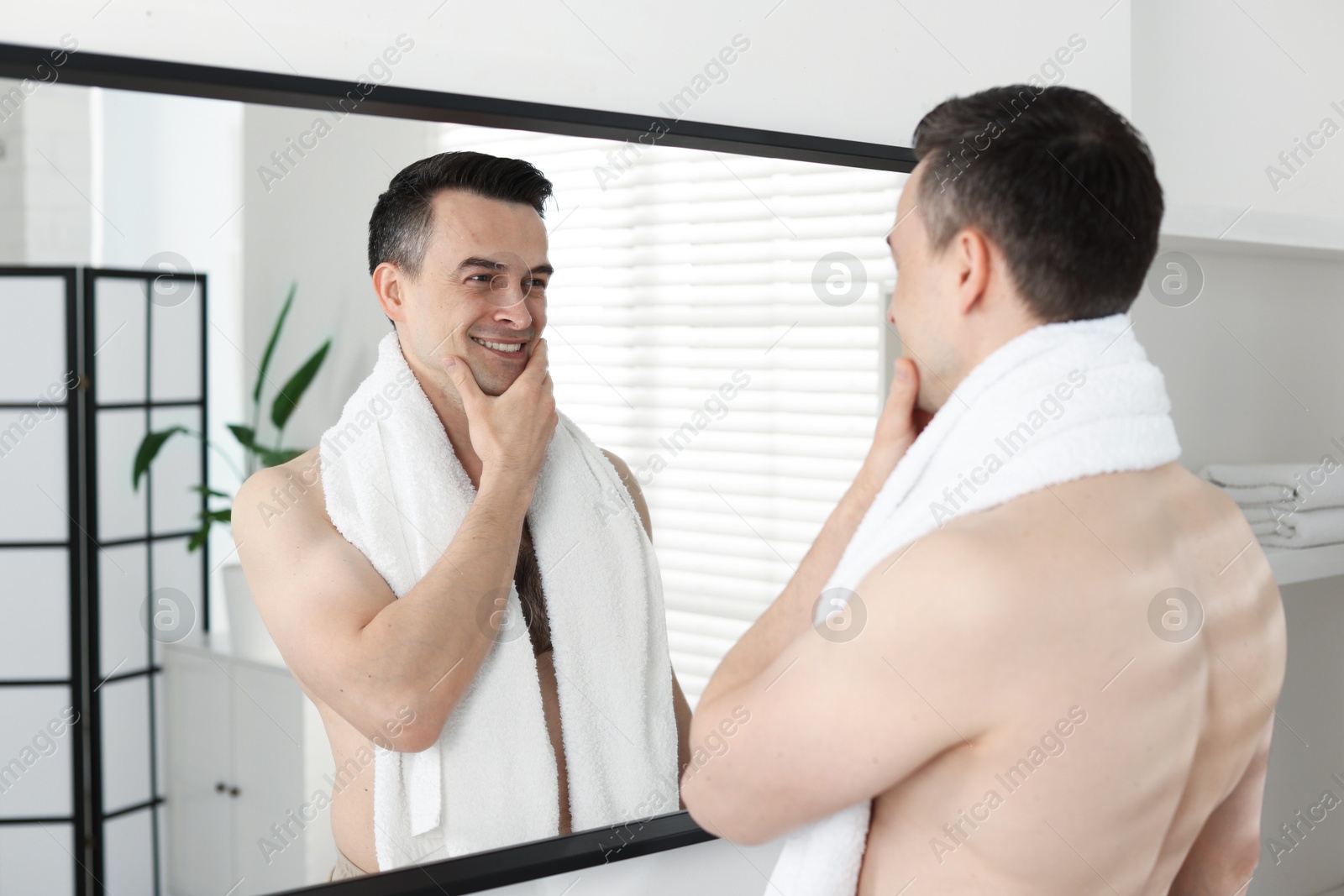Photo of Smiling man after shaving looking at mirror in bathroom