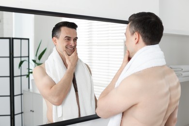 Photo of Smiling man after shaving looking at mirror in bathroom