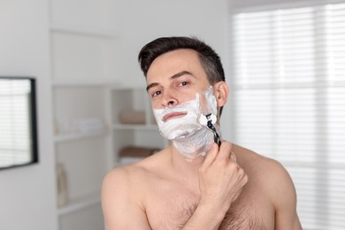 Photo of Handsome man shaving with razor at home