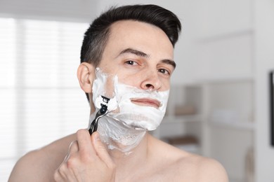 Photo of Handsome man shaving with razor at home