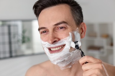 Photo of Smiling man shaving with razor at home