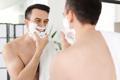 Photo of Smiling man applying shaving foam near mirror in bathroom