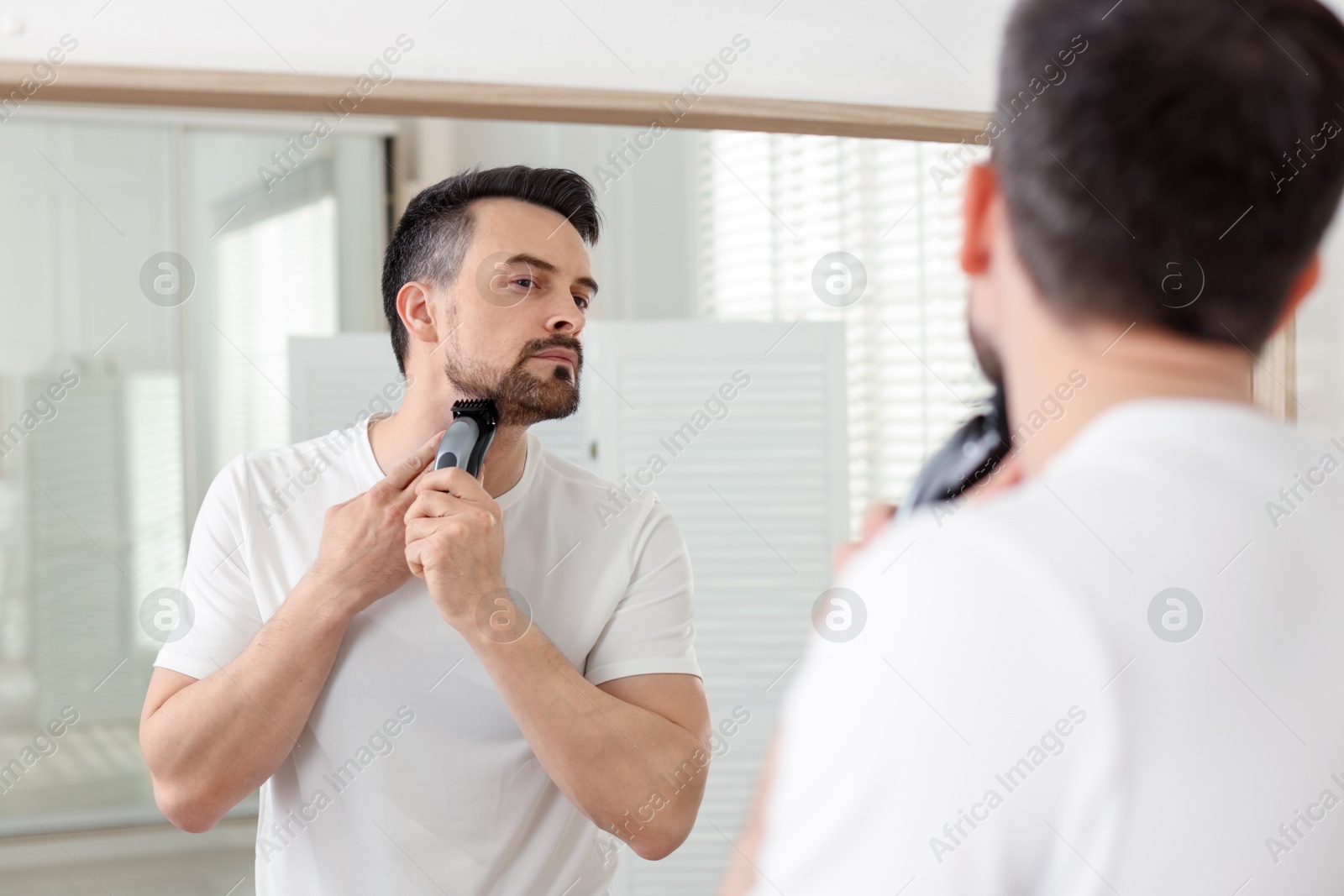 Handsome man shaving with trimmer near mirror at home Photo of Handsome man shaving with trimmer near mirror at home