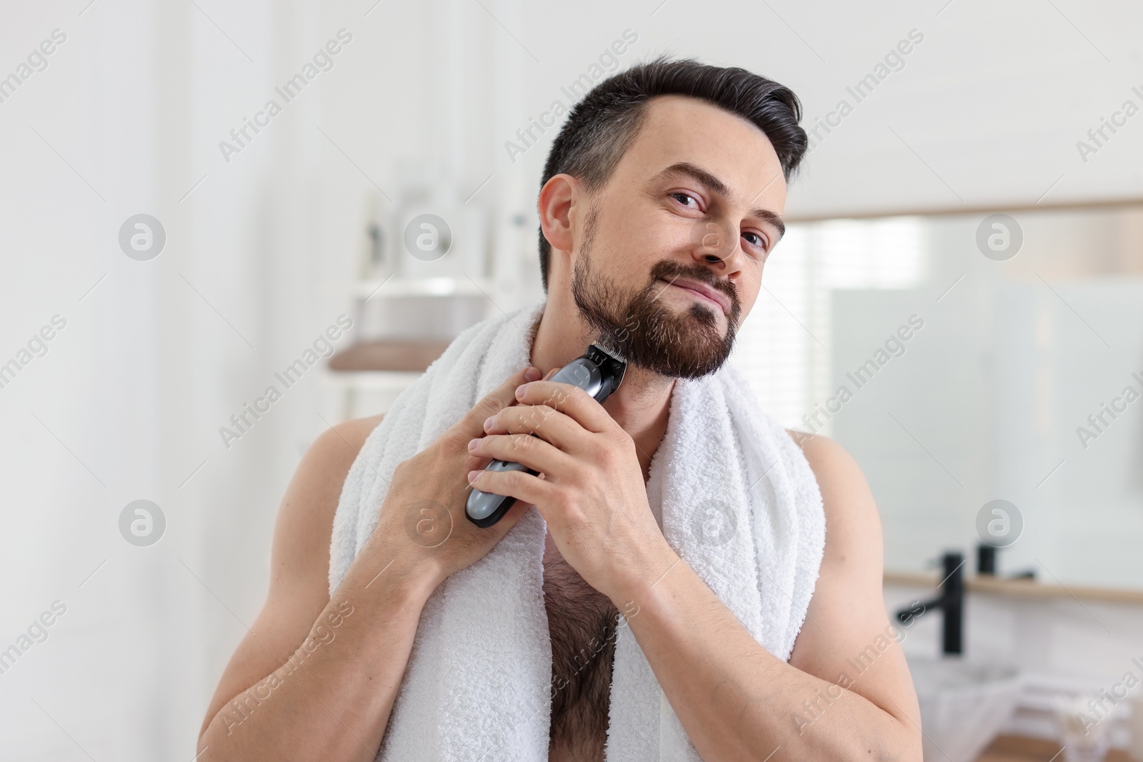 Handsome man shaving with trimmer in bathroom Photo of Handsome man shaving with trimmer in bathroom