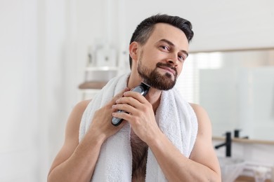 Photo of Handsome man shaving with trimmer in bathroom