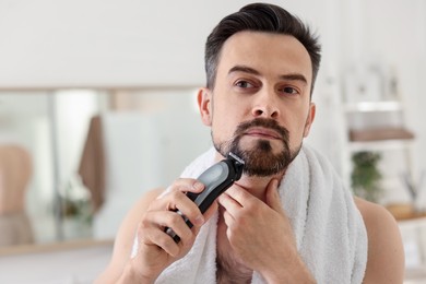Photo of Handsome man shaving with trimmer in bathroom