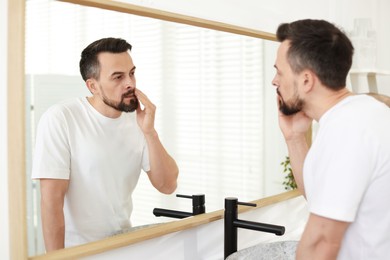 Photo of Handsome man before shaving looking at mirror in bathroom