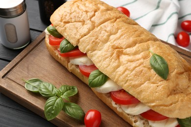Photo of Tasty sandwich with mozzarella cheese, tomatoes and basil on black wooden table, closeup