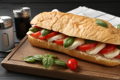 Photo of Tasty sandwich with mozzarella cheese, tomatoes and basil on black wooden table, closeup