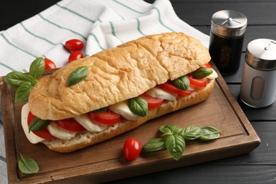 Photo of Tasty sandwich with mozzarella cheese, tomatoes and basil on black wooden table, closeup