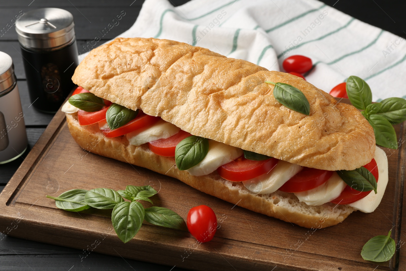 Tasty sandwich with mozzarella cheese, tomatoes and basil on black wooden table, closeup Photo of Tasty sandwich with mozzarella cheese, tomatoes and basil on black wooden table, closeup