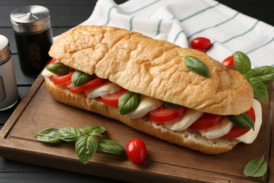Photo of Tasty sandwich with mozzarella cheese, tomatoes and basil on black wooden table, closeup