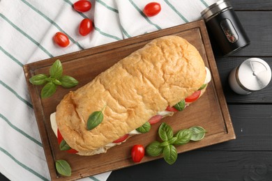 Photo of Tasty sandwich with mozzarella cheese, tomatoes, basil and spices on black wooden table, flat lay