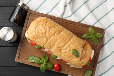 Photo of Tasty sandwich with mozzarella cheese, tomatoes, basil and spices on black wooden table, flat lay