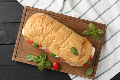 Photo of Tasty sandwich with mozzarella cheese, tomatoes and basil on black wooden table, top view