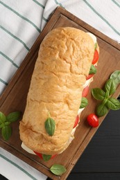 Photo of Tasty sandwich with mozzarella cheese, tomatoes and basil on black wooden table, top view