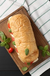 Photo of Tasty sandwich with mozzarella cheese, tomatoes and basil on black wooden table, top view
