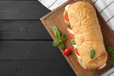 Photo of Tasty sandwich with mozzarella cheese, tomatoes and basil on black wooden table, top view. Space for text