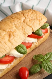 Photo of Tasty sandwich with mozzarella cheese, tomatoes and basil on table, closeup