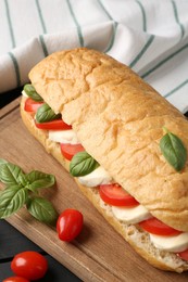 Photo of Tasty sandwich with mozzarella cheese, tomatoes and basil on black wooden table, closeup