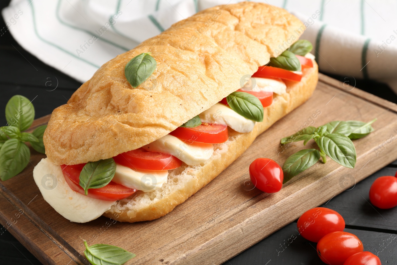 Tasty sandwich with mozzarella cheese, tomatoes and basil on black wooden table, closeup Photo of Tasty sandwich with mozzarella cheese, tomatoes and basil on black wooden table, closeup