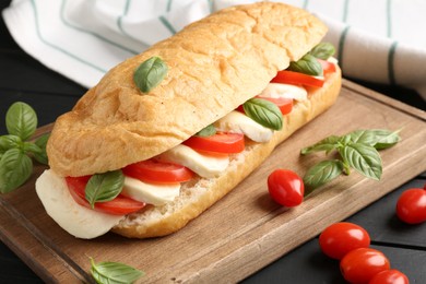Photo of Tasty sandwich with mozzarella cheese, tomatoes and basil on black wooden table, closeup