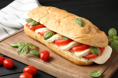 Photo of Tasty sandwich with mozzarella cheese, tomatoes and basil on black wooden table, closeup