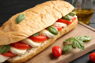 Photo of Tasty sandwich with mozzarella cheese, tomatoes and basil on black wooden table, closeup