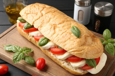 Photo of Tasty sandwich with mozzarella cheese, tomatoes and basil on black wooden table, closeup