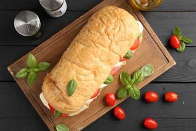 Photo of Tasty sandwich with mozzarella cheese, tomatoes, basil and spices on black wooden table, flat lay